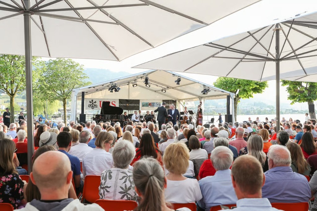 Publikum auf orangen Stühlen vor der Open-Air-Bühne am Zürichsee